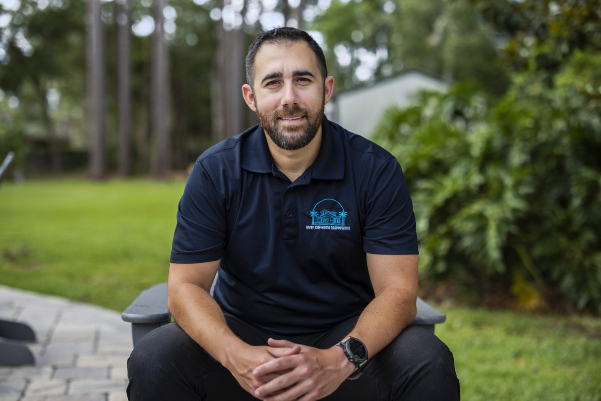 Wade Hosseini, owner and inspector at River City Home Inspections, seated outdoors in a navy River City polo